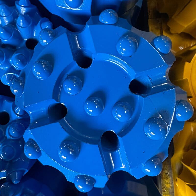A variety of DTH drill bits arranged on a wooden workbench