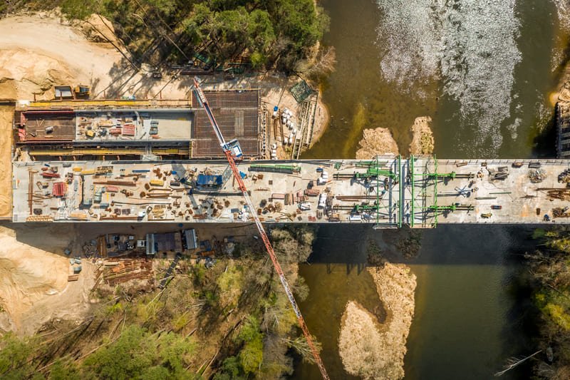 A construction site featuring workers and machinery building a large bridge over a river, showcasing engineering progress.
