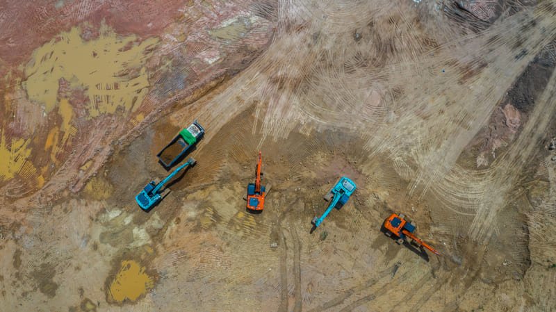 A drilling site featuring heavy machinery, workers in safety gear, and equipment set against a rugged landscape.