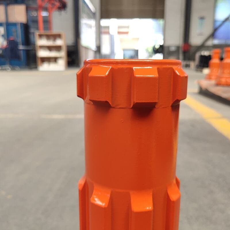 Close-up of an orange DTH bit, showcasing its intricate design and sharp cutting edges for drilling applications.