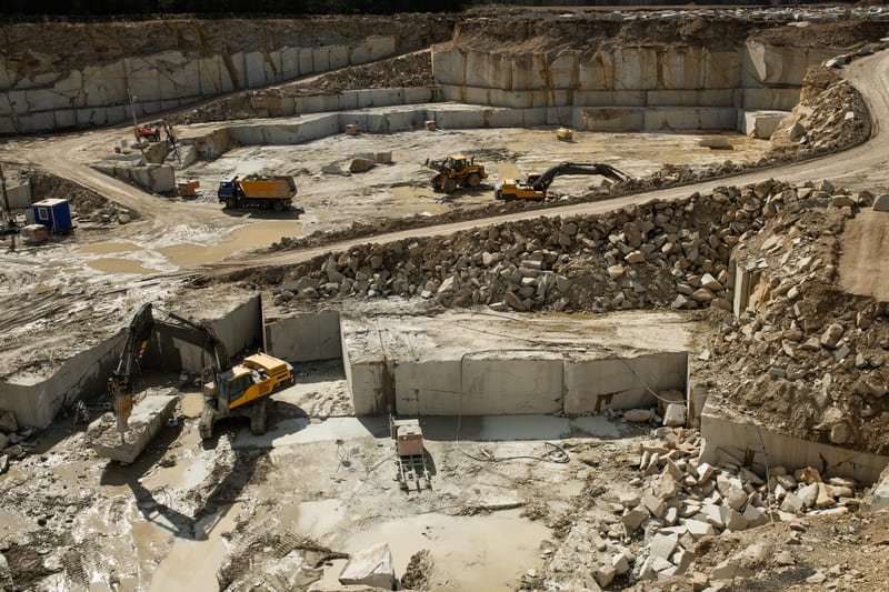 Aerial view of a quarrying site showcasing large machinery and rock formations in a rugged landscape.