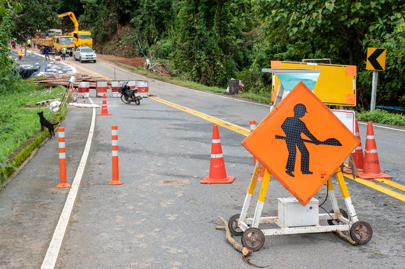 A construction site featuring heavy machinery and workers engaged in road building activities, with safety barriers in place.