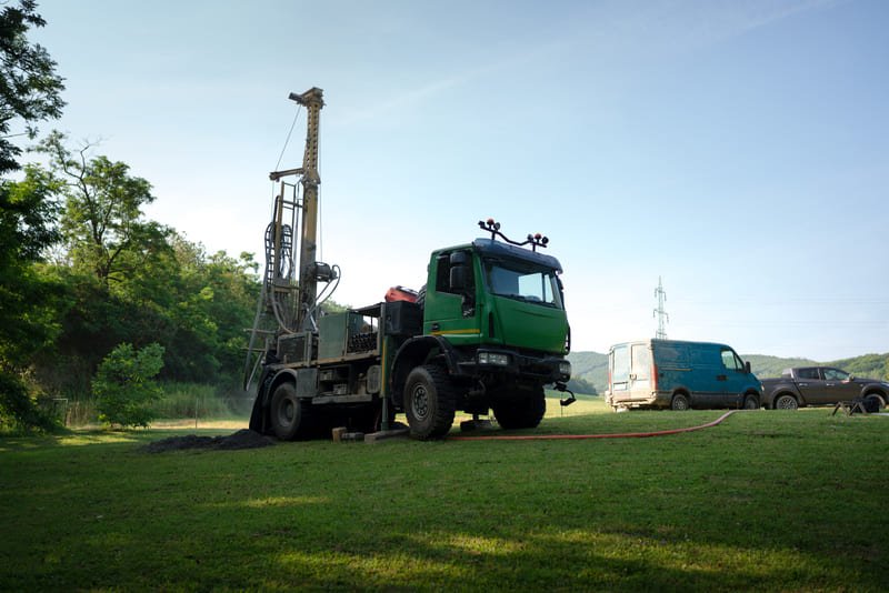 A drilling rig operating in rugged terrain with dust clouds